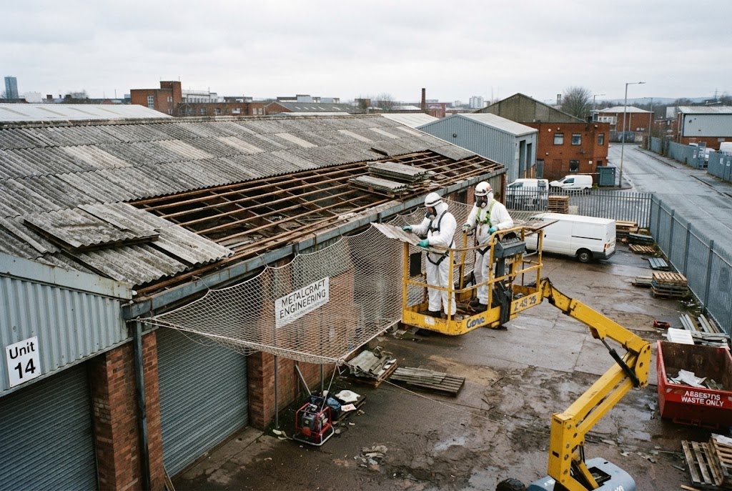 Two operatives on a mobile platform removing asbestos cement roof sheets from an industrial unit with a safety net